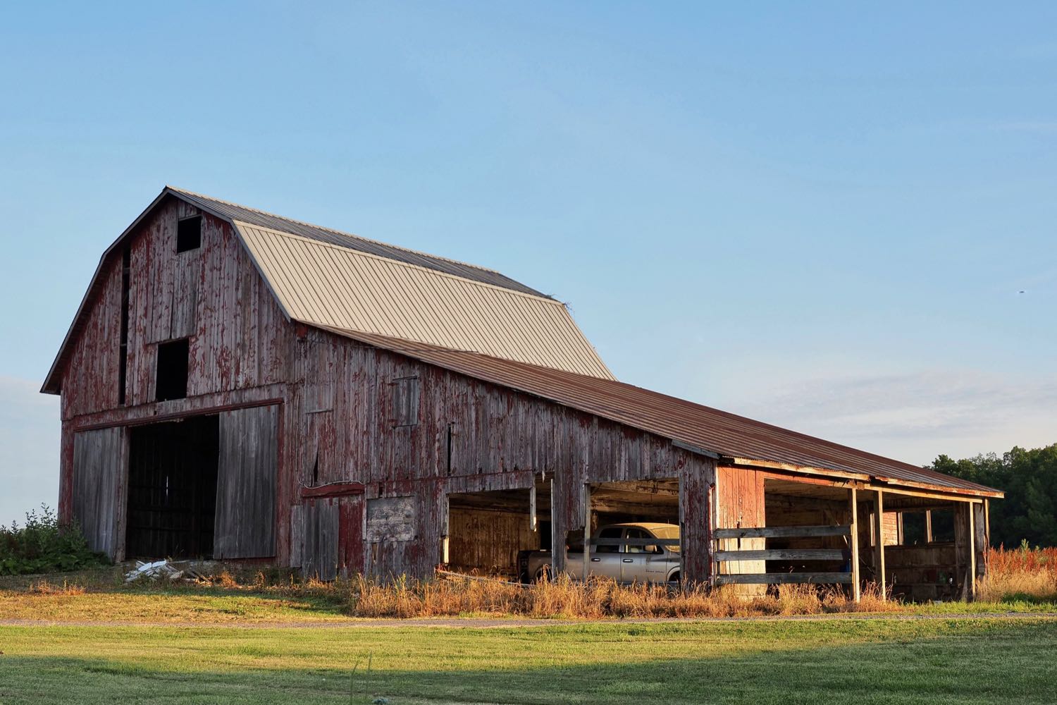 An old barn, weathered wood, faded and peeling red paint, metal roof, in morning light.