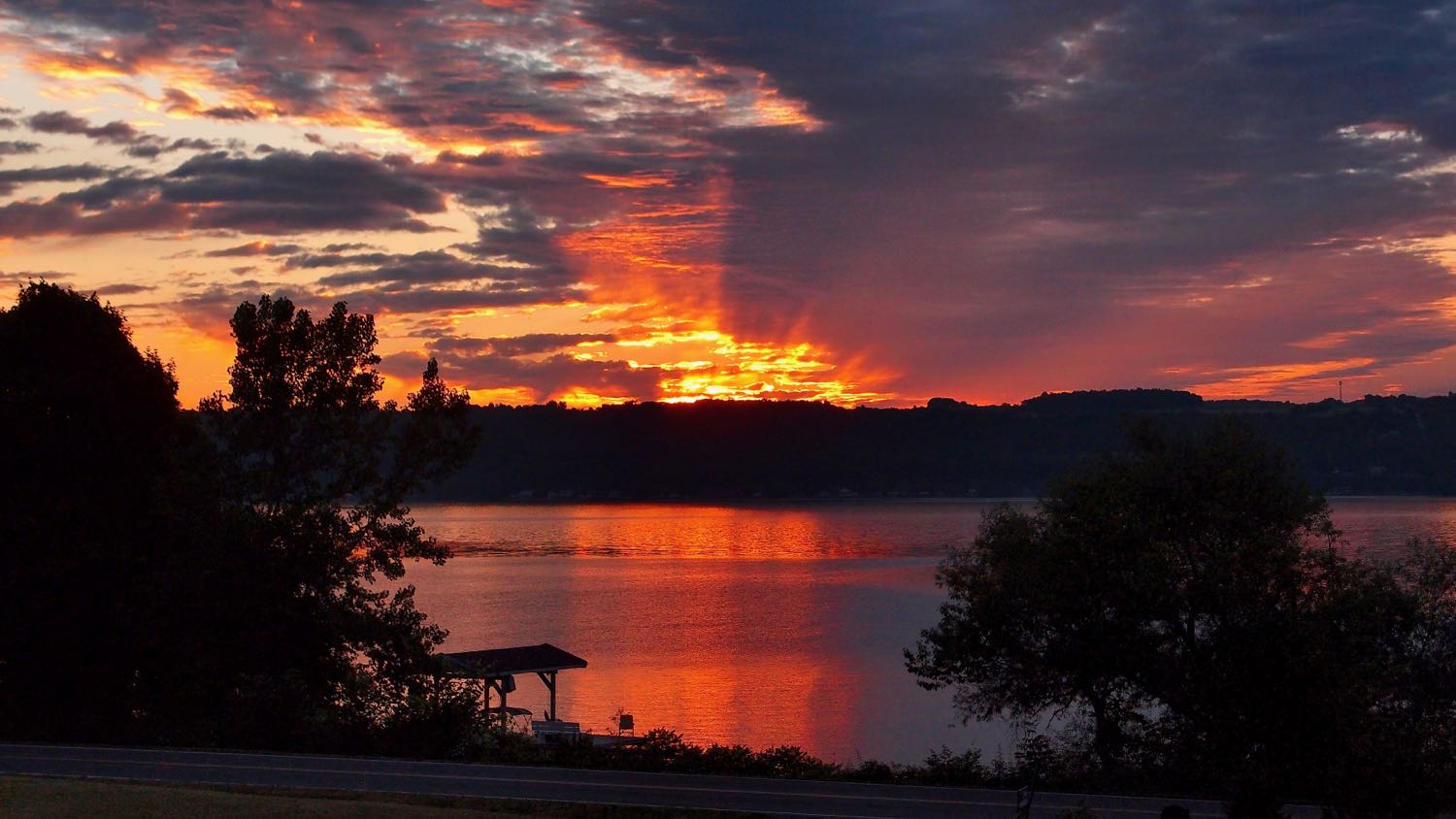 Clouds illuminated in red from the sun just below the horizon, reflected in the lake.