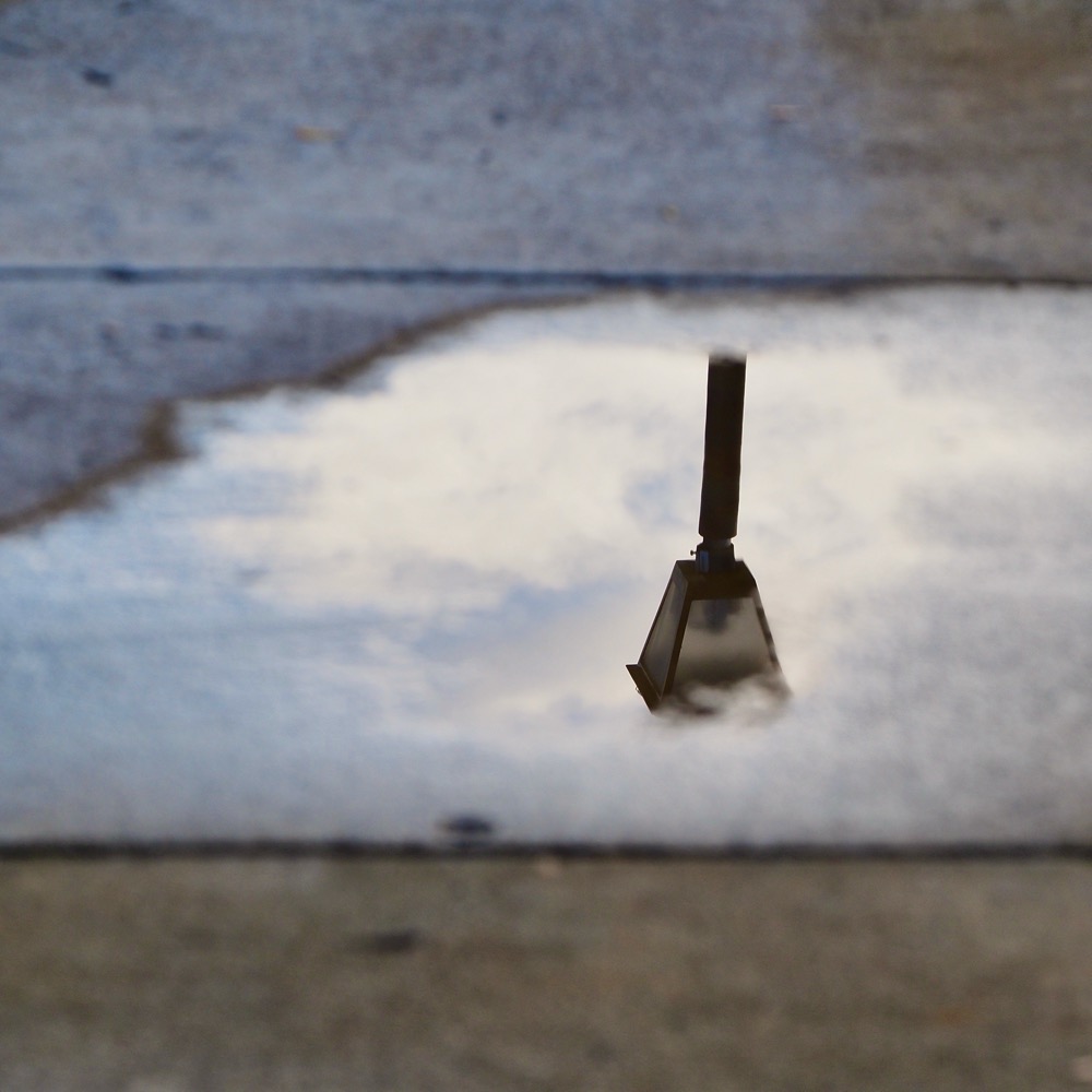Photo of a street lamp reflected in a puddle on the sidewalk