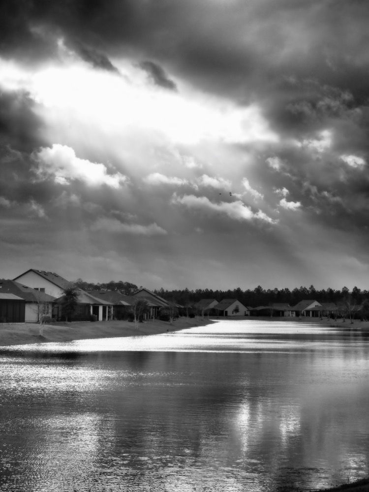 An opening in the clouds admits sunlight, which is reflected on the pond.