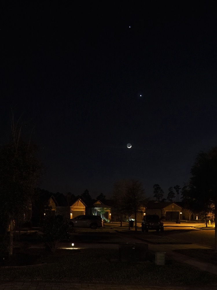 A crescent moon, Venus and Jupiter in near vertical alignment ascending above the horizon in a suburban Florida street scene.