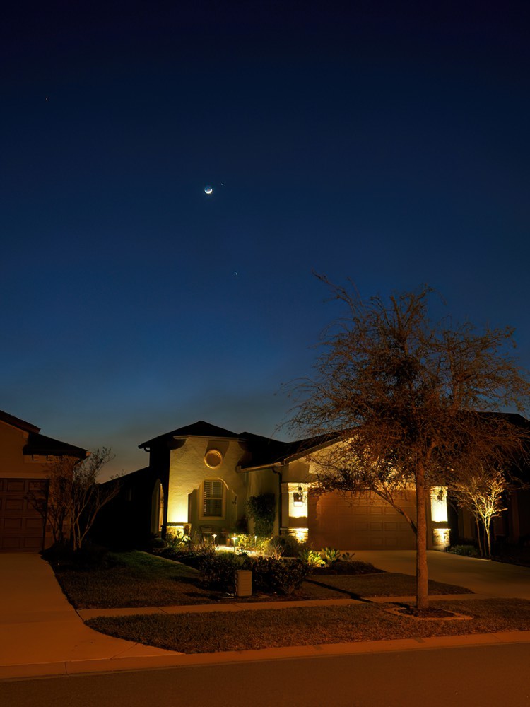 Crescent moon, near Jupiter and above Venus in the sky above a suburban Florida house.