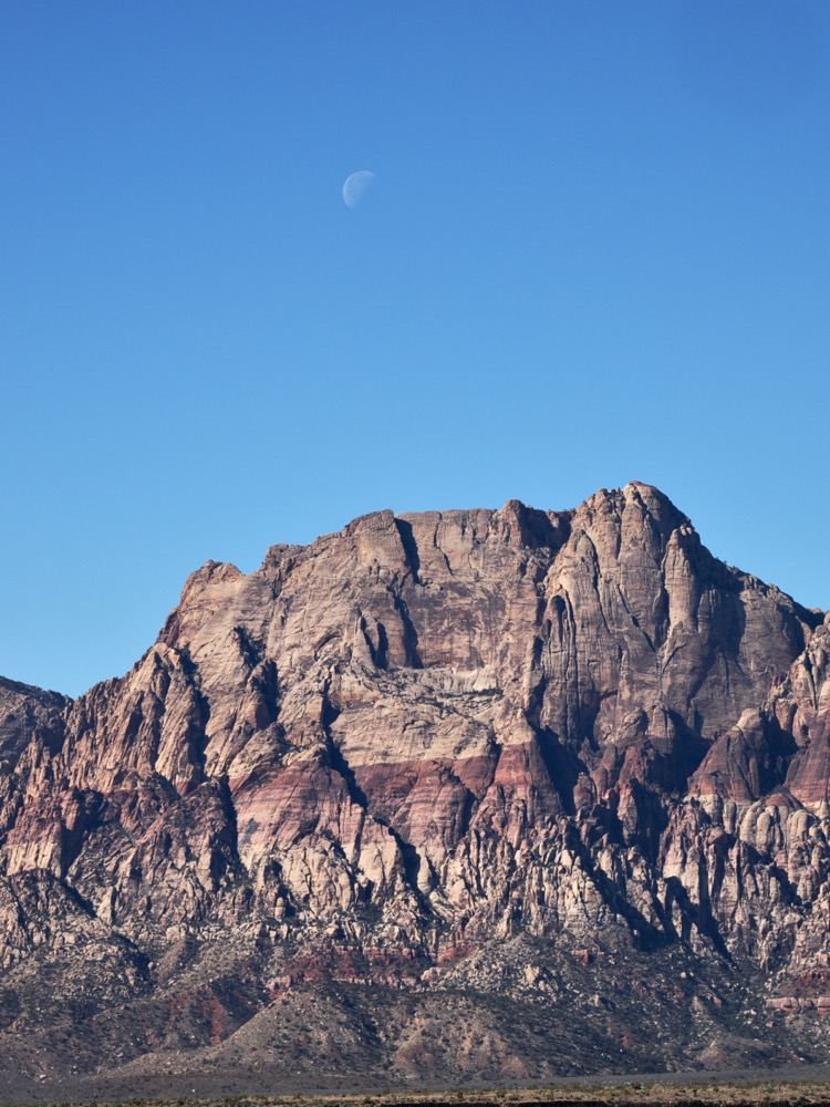 Half moon visible over stratified rock formation in Red Rocks Nevada