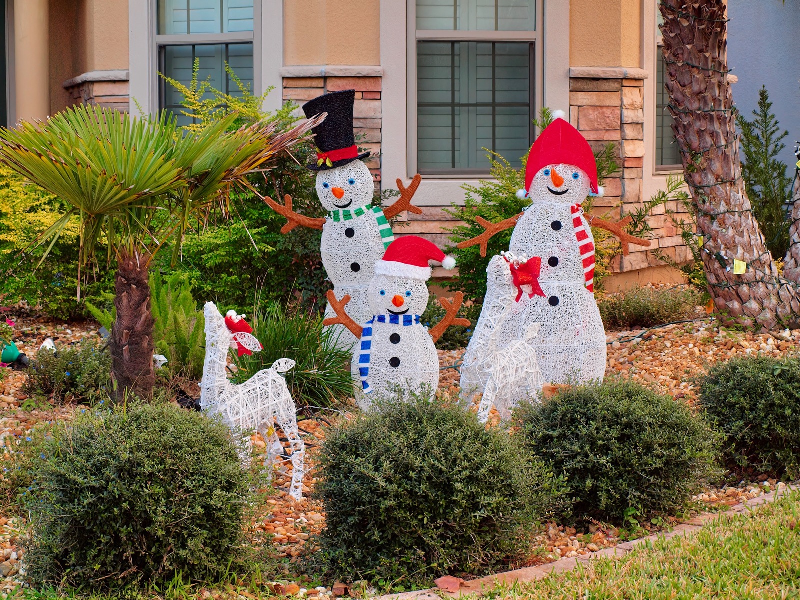 Three white plastic snow people and two white plastic reindeer in winter attire.