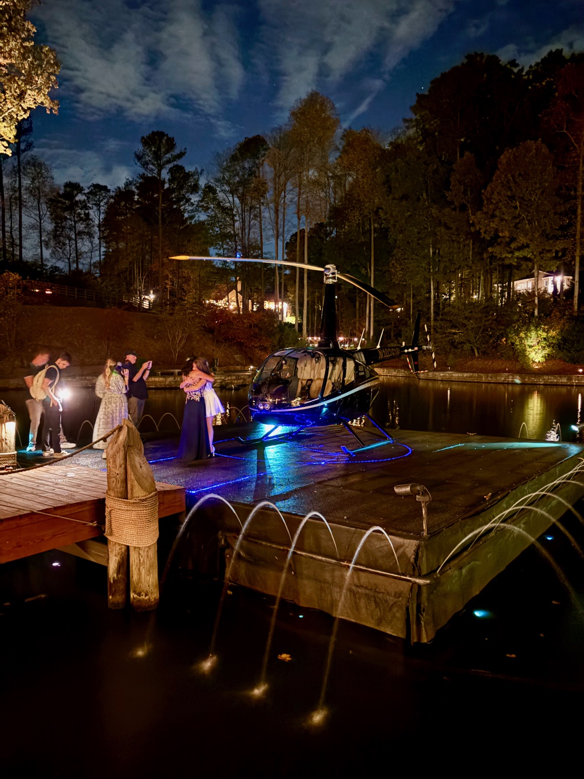 Bride and mother embracing on a floating helipad at night in a wedding venue.