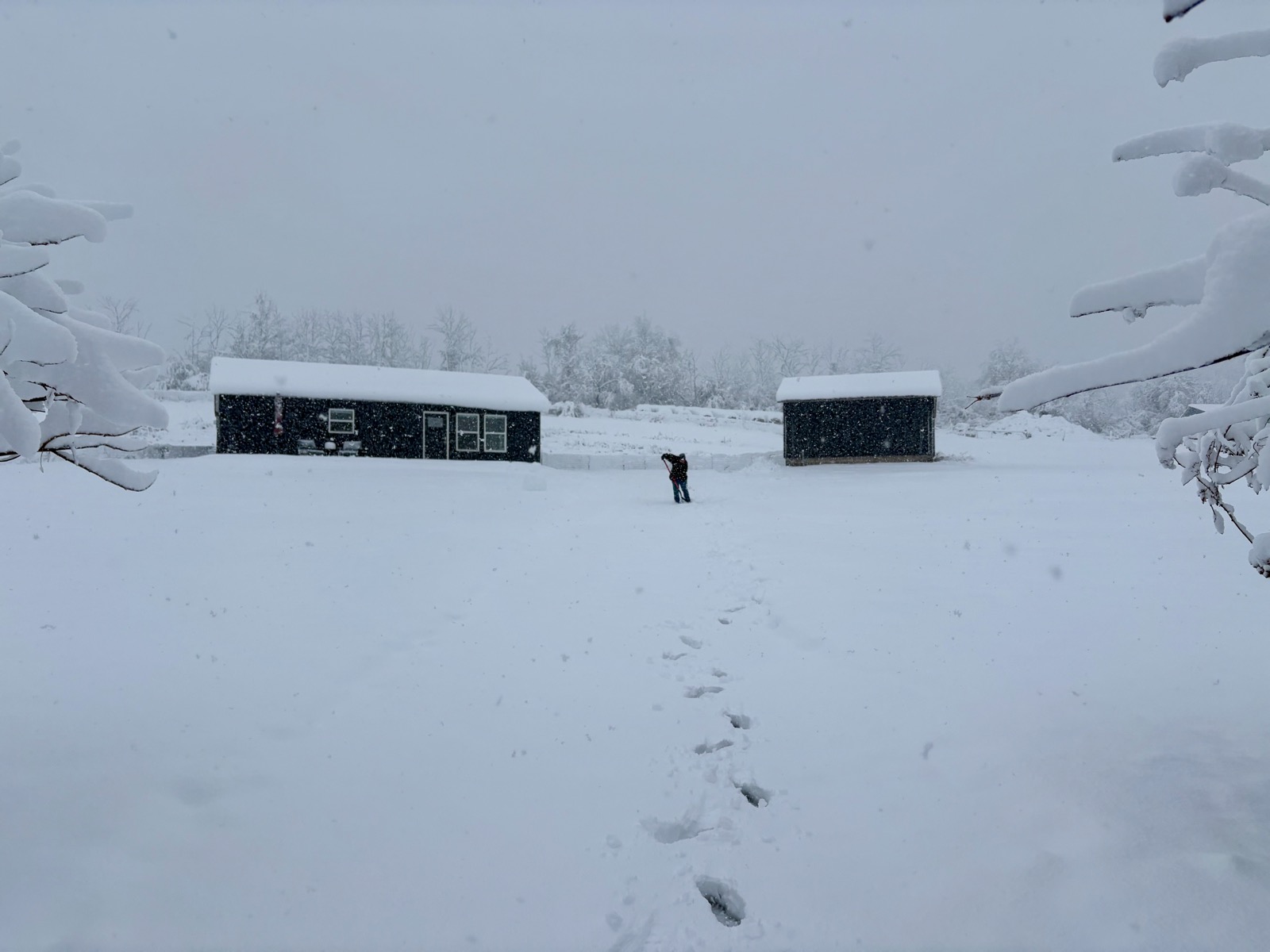 Photo of a rural house and garage in a snowscape with a person shoveling snow