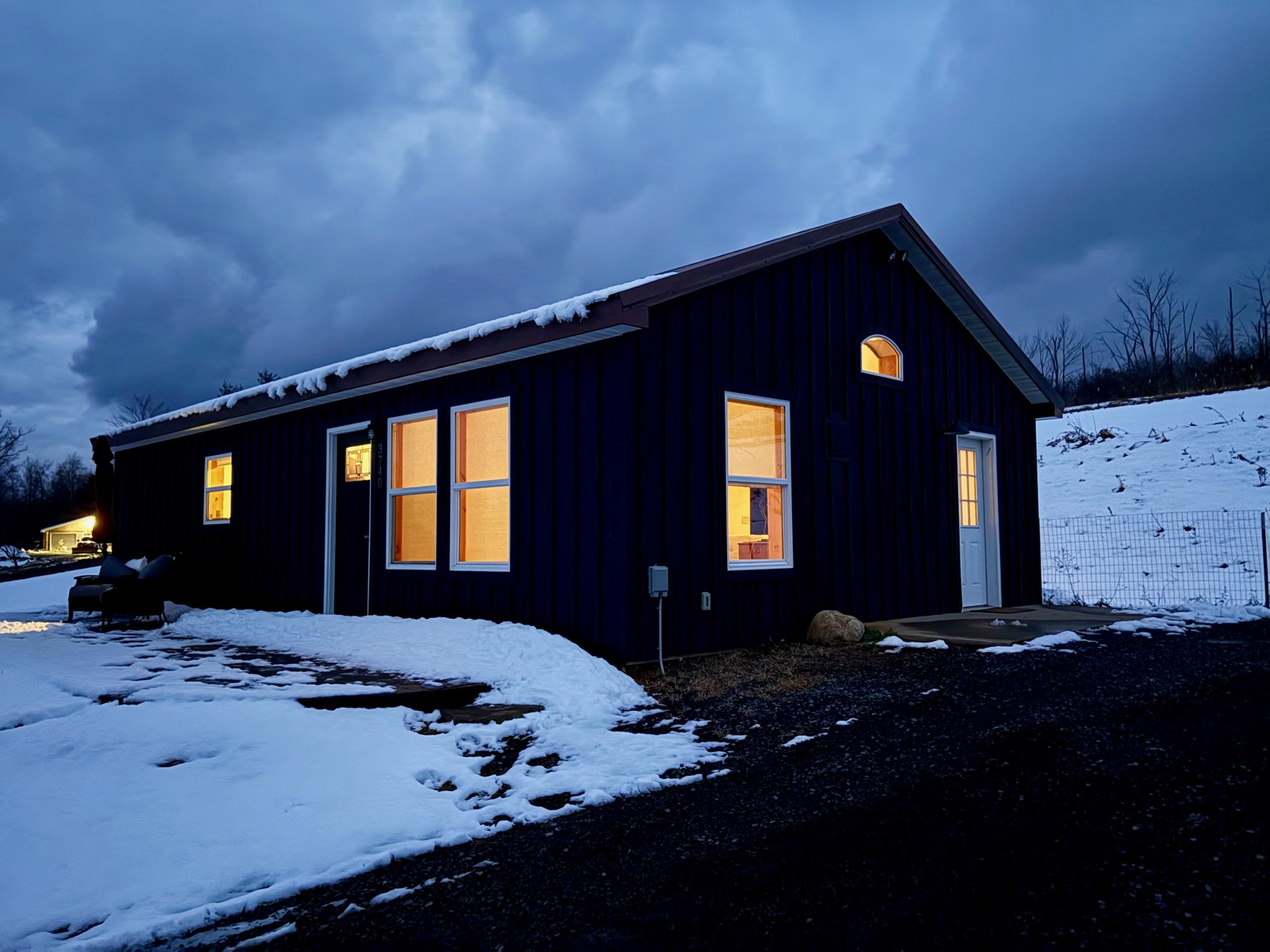 Three-quarter view of a house in the snow with the lights on in cloudy early morning twilight