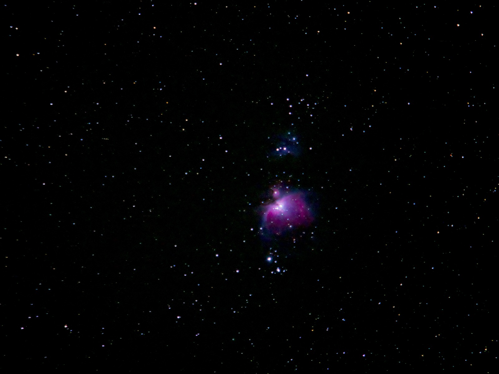Photo of the Orion Nebula, a small purple-ish fuzzball amid a background of stars