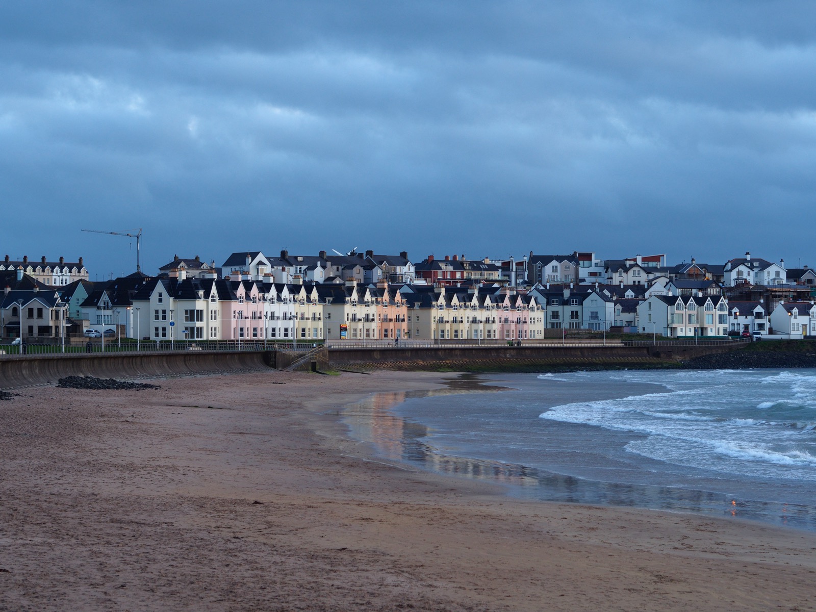 Shot of some rowhouses along the sea shore in Northern Ireland in low-angle light beneath a gray sky.