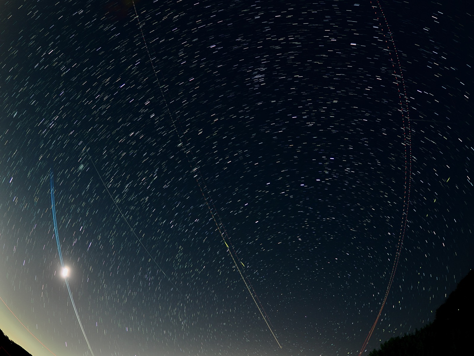 Light trail of a series of Starlink satellites passing before a crescent moon