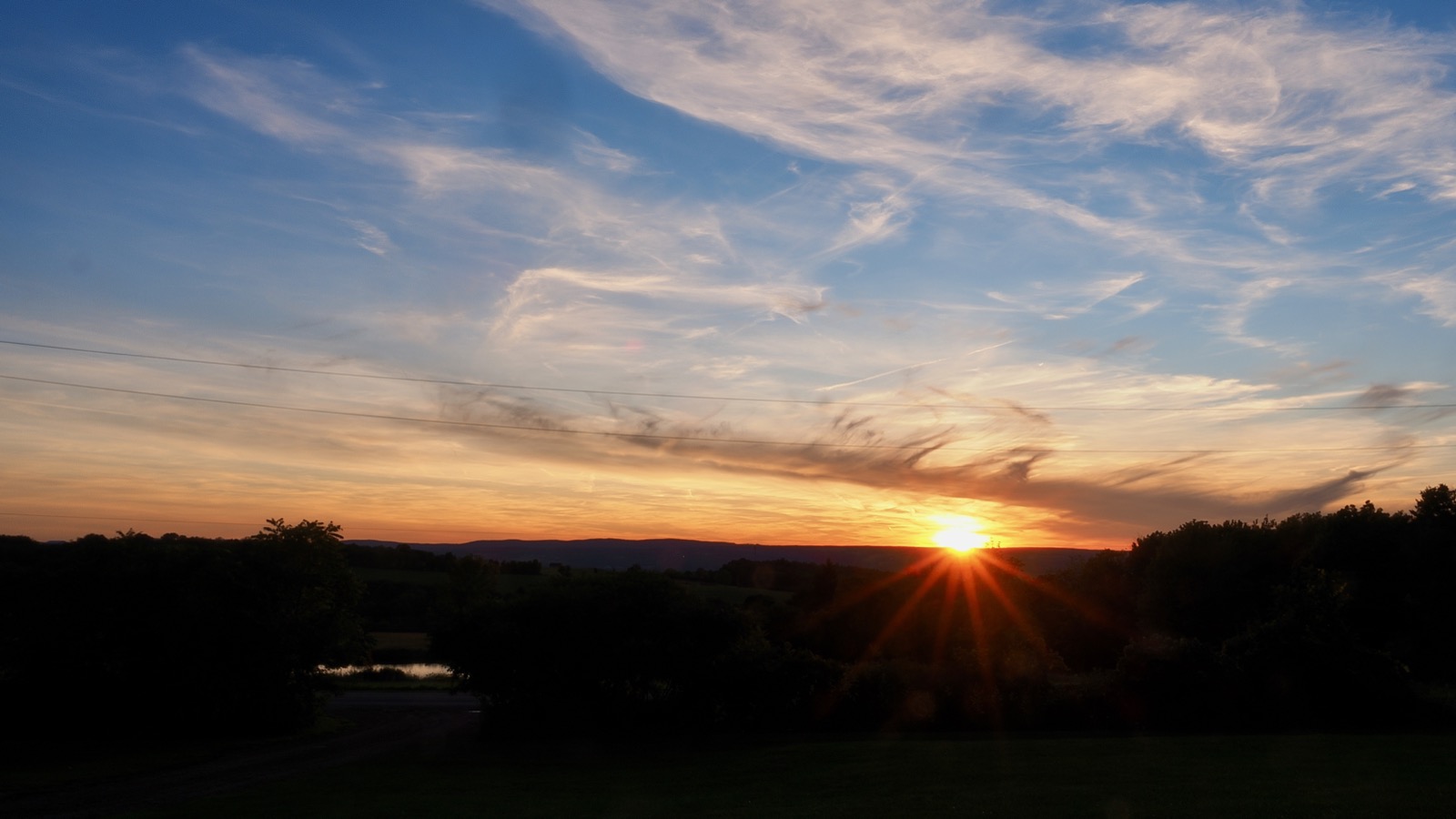 Starburst effect around the setting sun against the horizon beneath some thin clouds