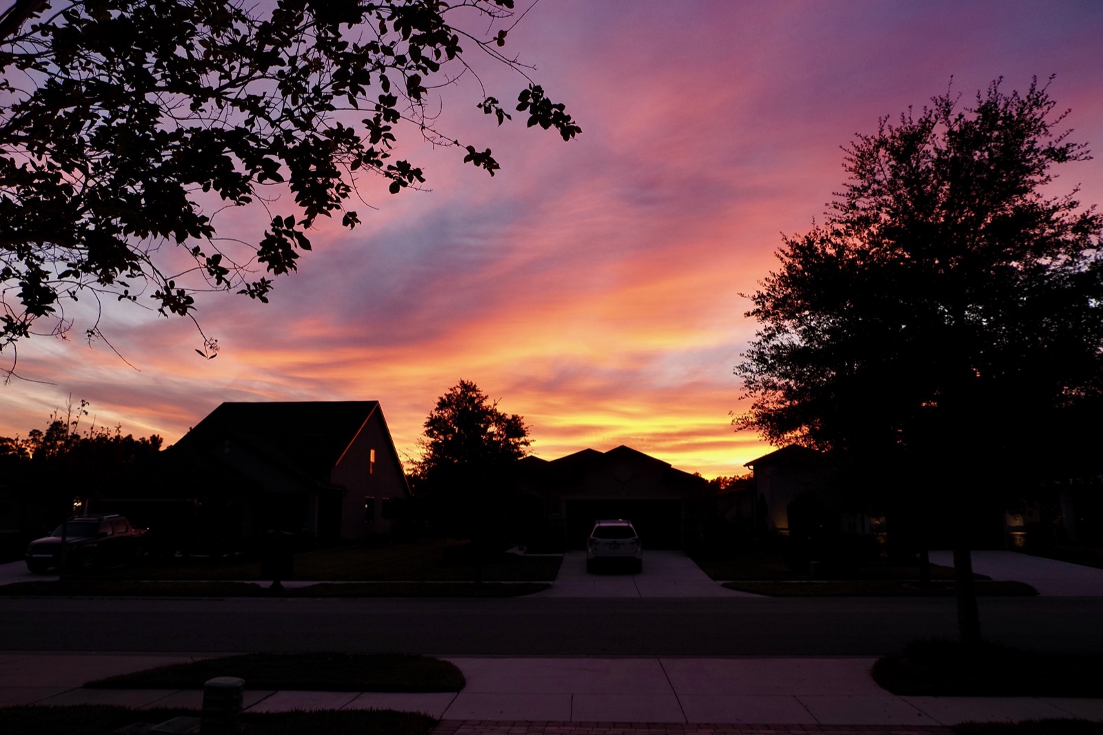 Clouds illuminated from below by the setting sun above a suburban landscape.