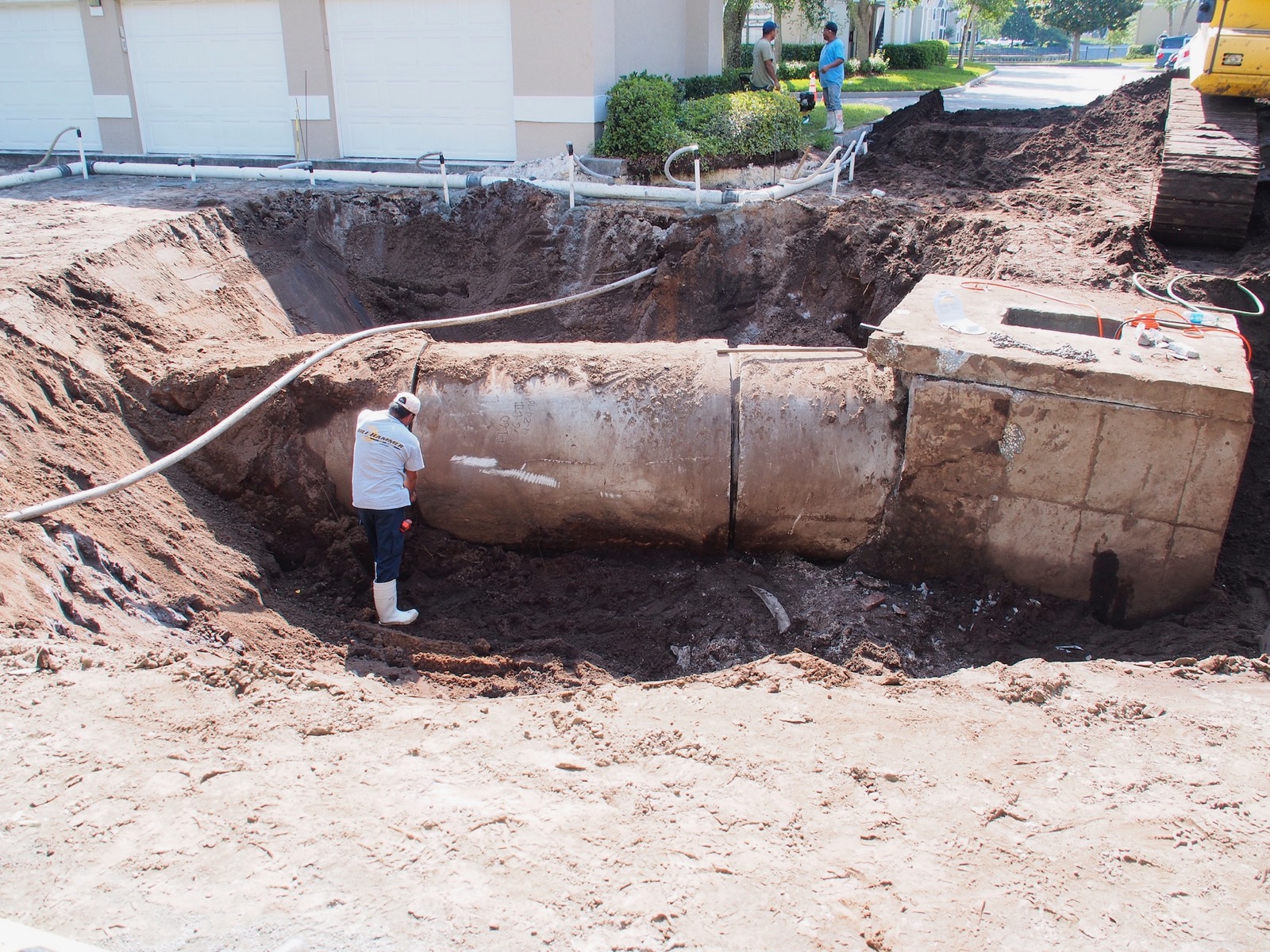 Backhoe excavating the earth surrounding a large drain pipe with a workman standing on the pipe.