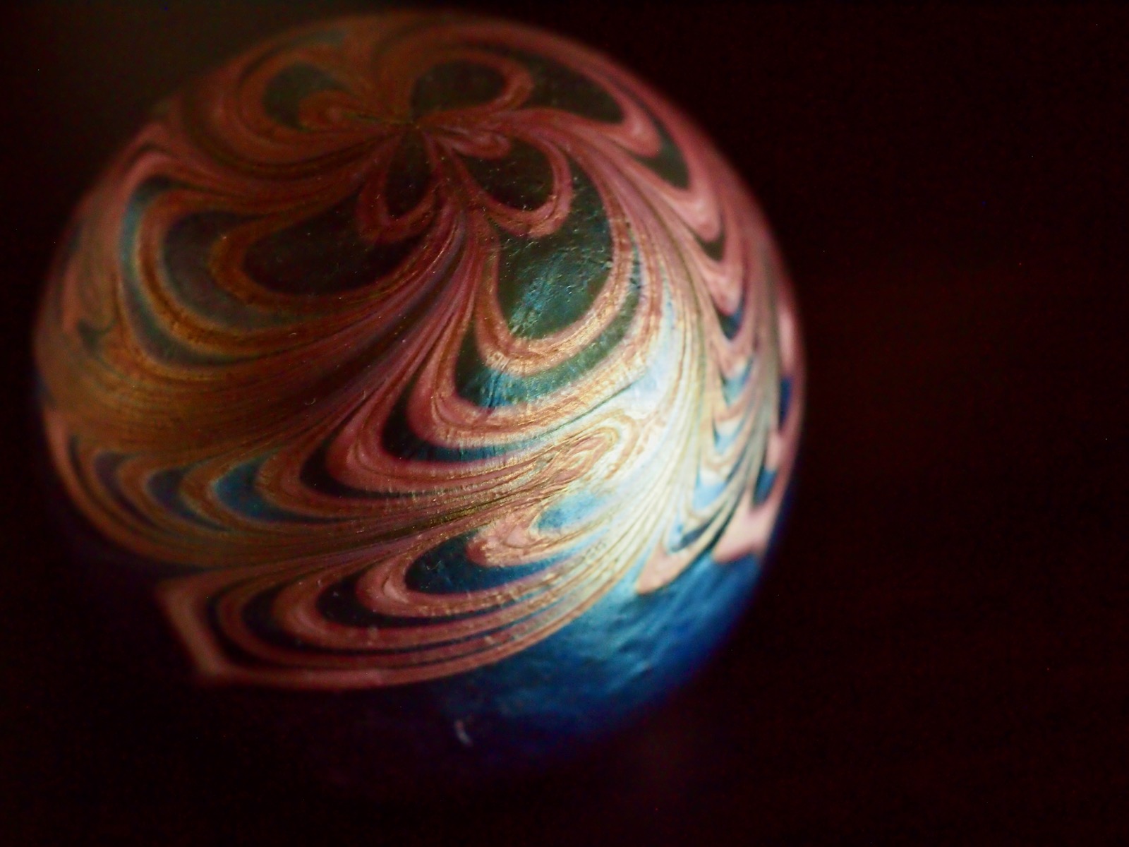 Closeup image of a small glass globe with metallic swirls against a black backdrop