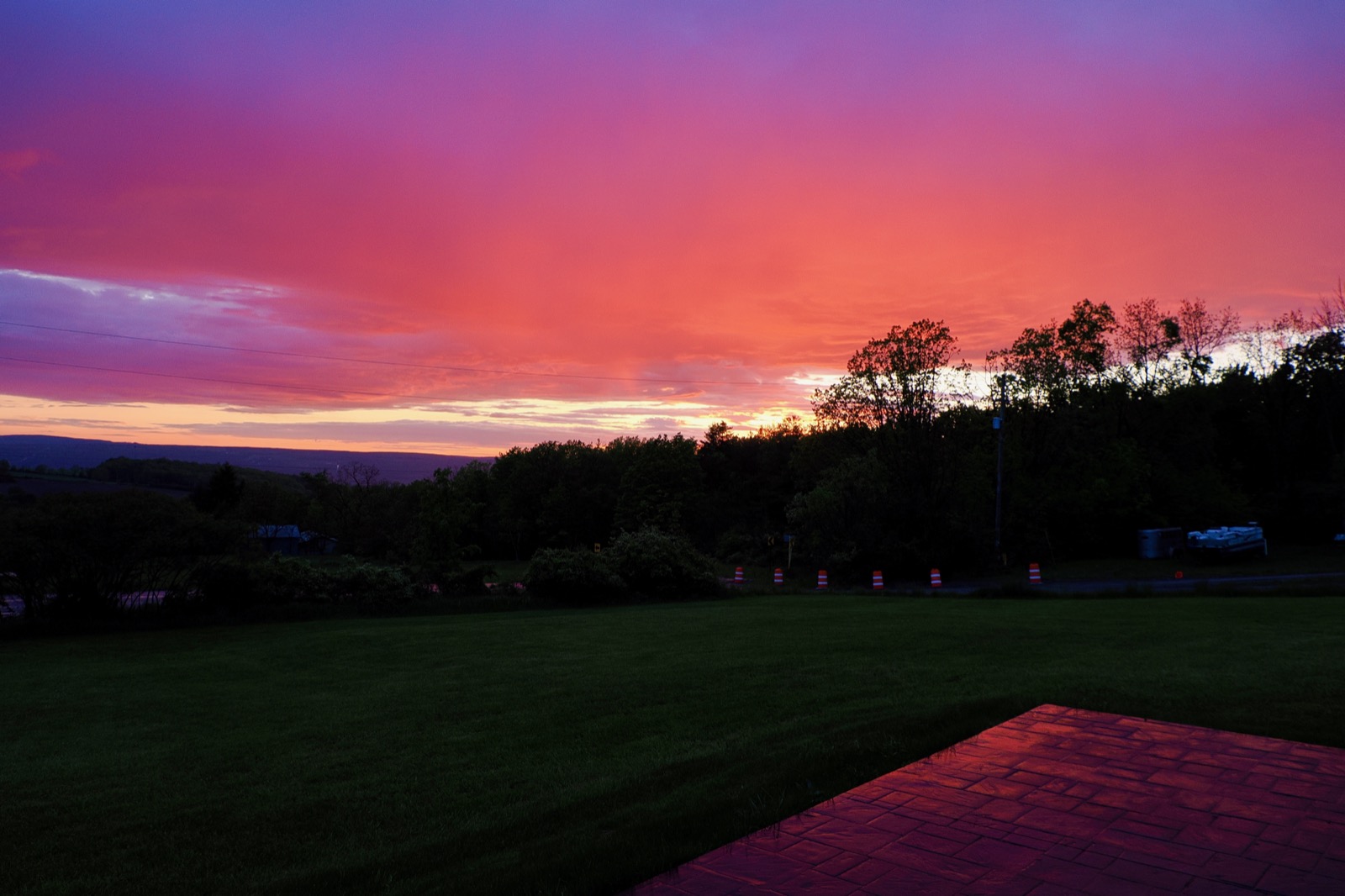 Distant clouds lilluminated in red from below by the setting sun, silhouetting some trees with a bit of the glow reflected on a wet porch