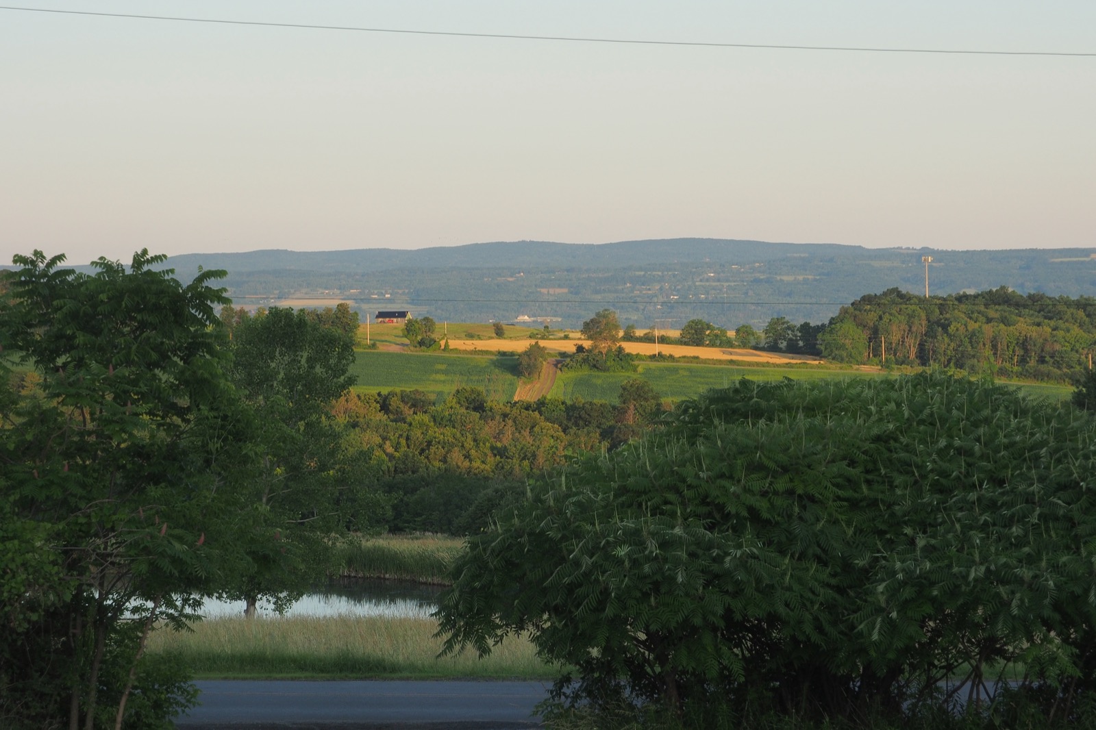 Medium telephoto image of farmland across a valley, with hills in the distance.