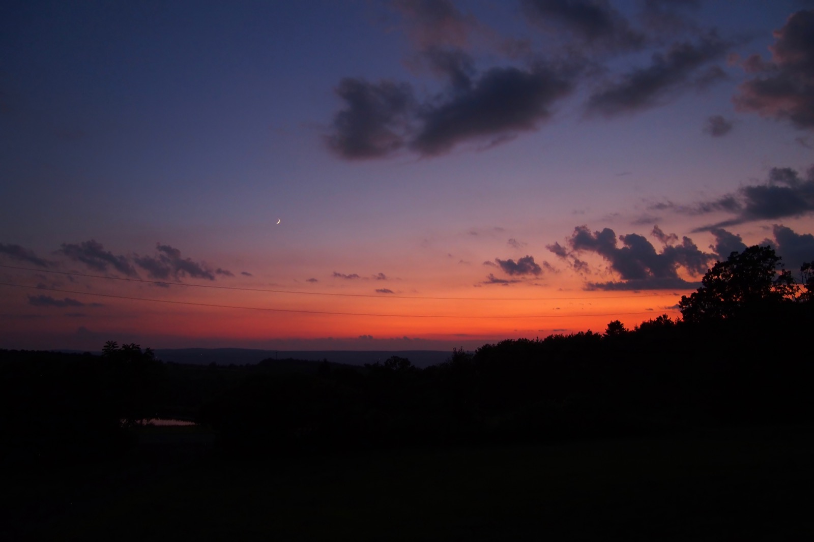 Crescent moon in a twilight sky with red and orange on the horizon. Annoying power lines are visible in the red and orange.