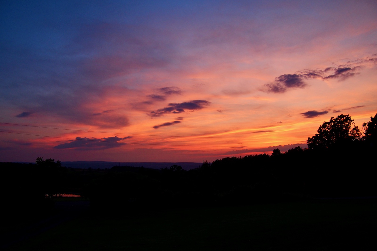 Evening twilight sky featuring red and yellow clouds illuminated from below by the setting sun against a dark horizon