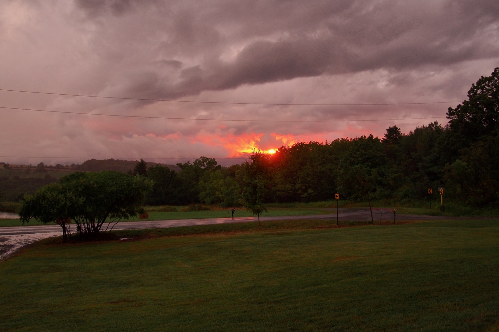 Sun setting behind storm clouds in a rural landscape.