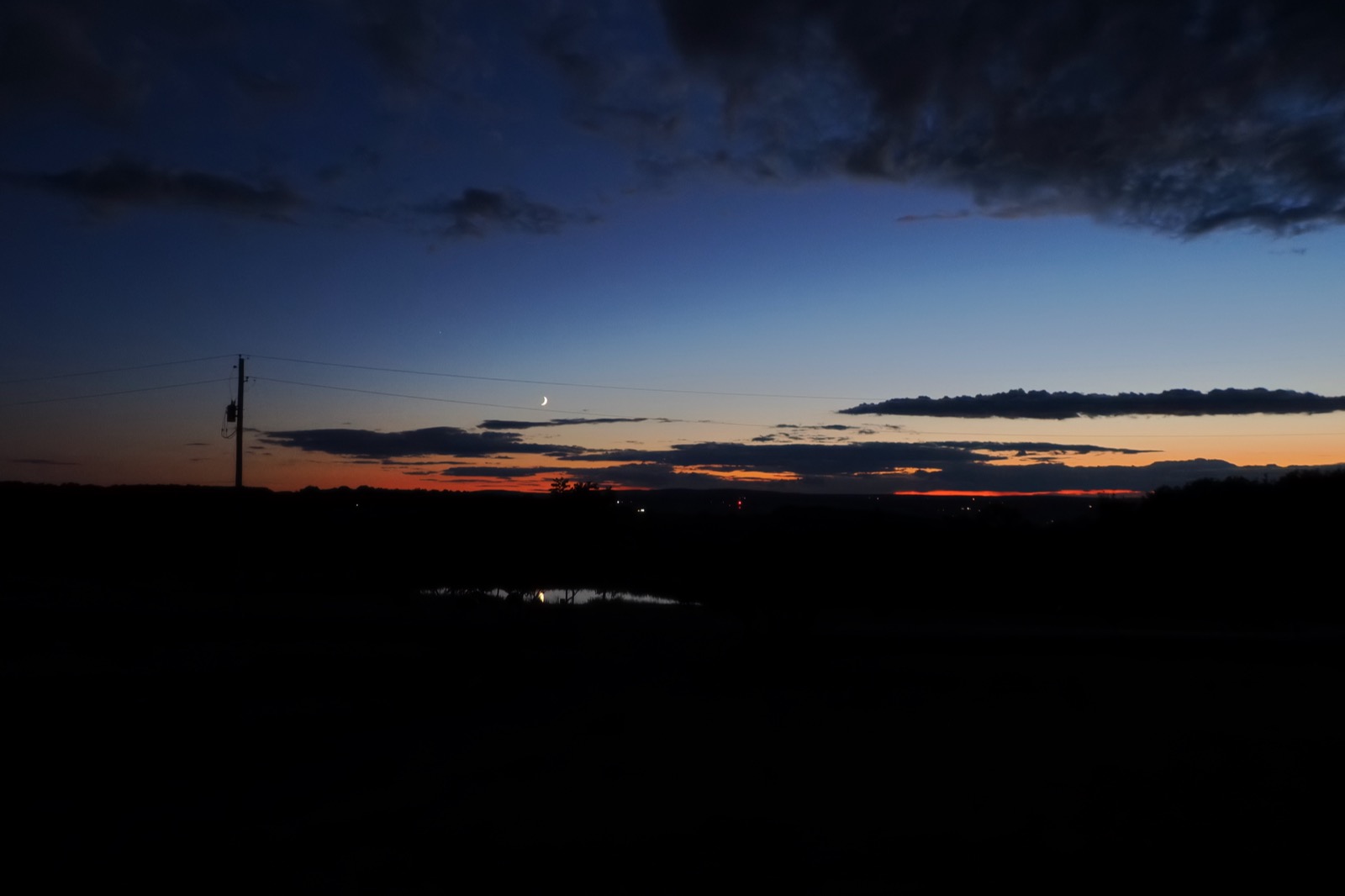 Evening twilight (blue hour) image of the waxing crescent moon descending to the horizon amidst clouds and a reddish glow along the horizon