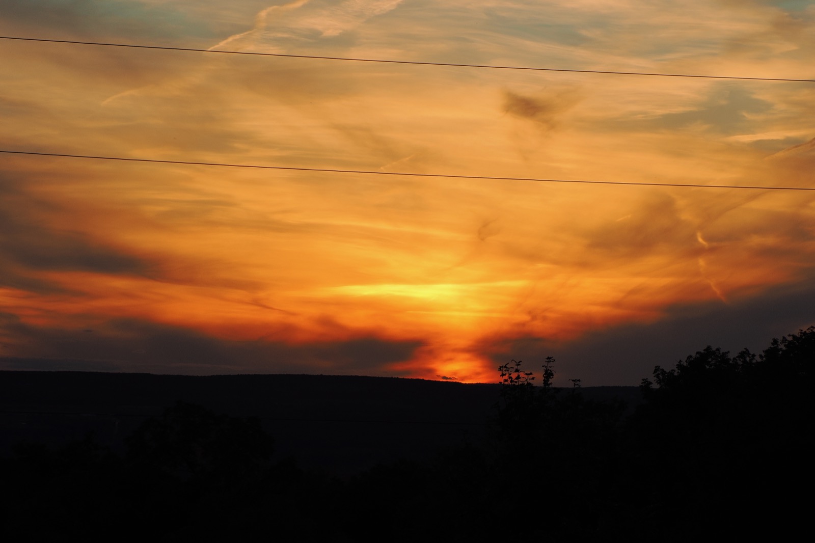 Red sky behind power lines against a horizon in silhouette