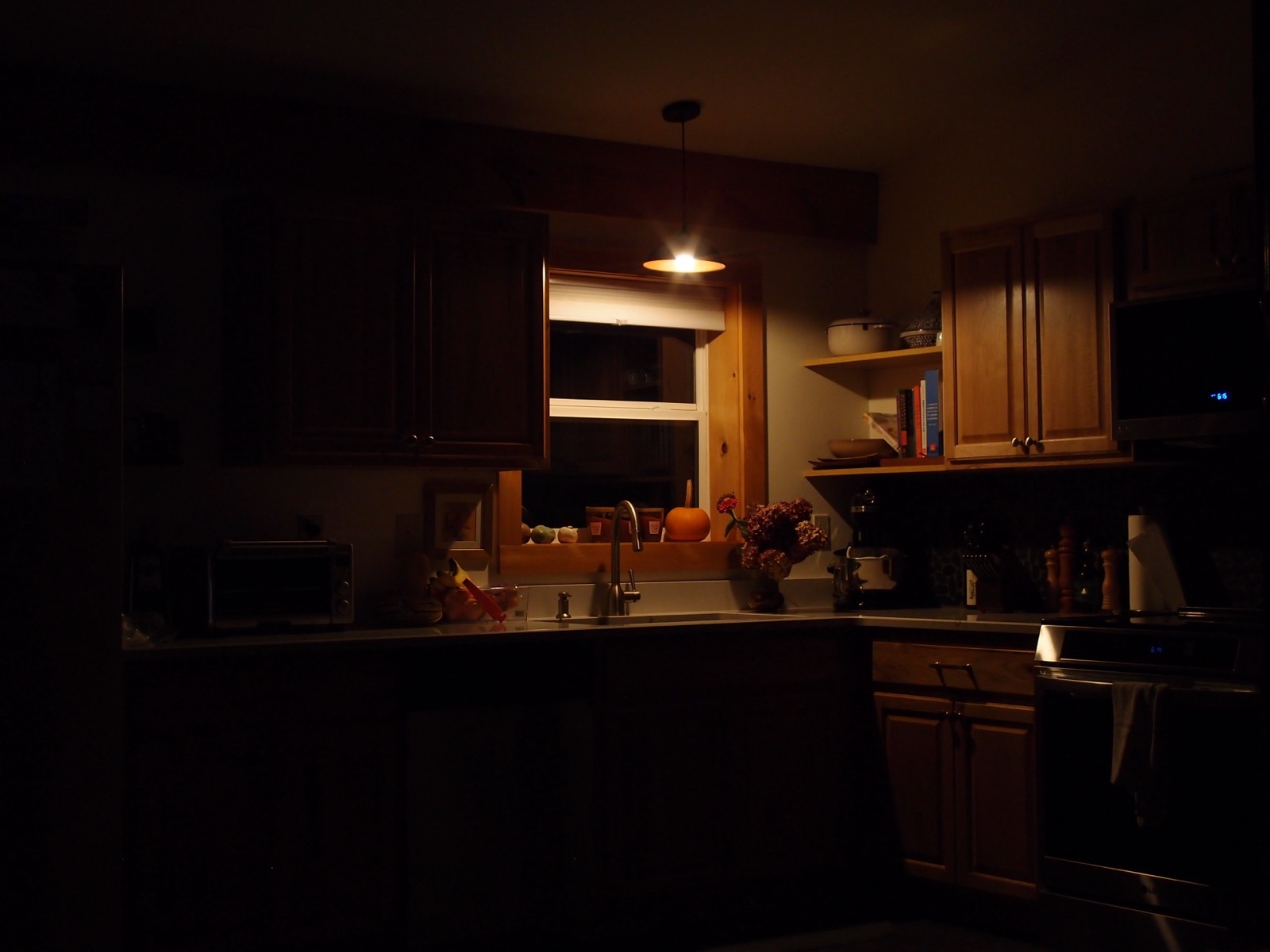 Photo of a kitchen sink, counter and some cabinets illuminated by a single overhead light in the early morning before sunrise