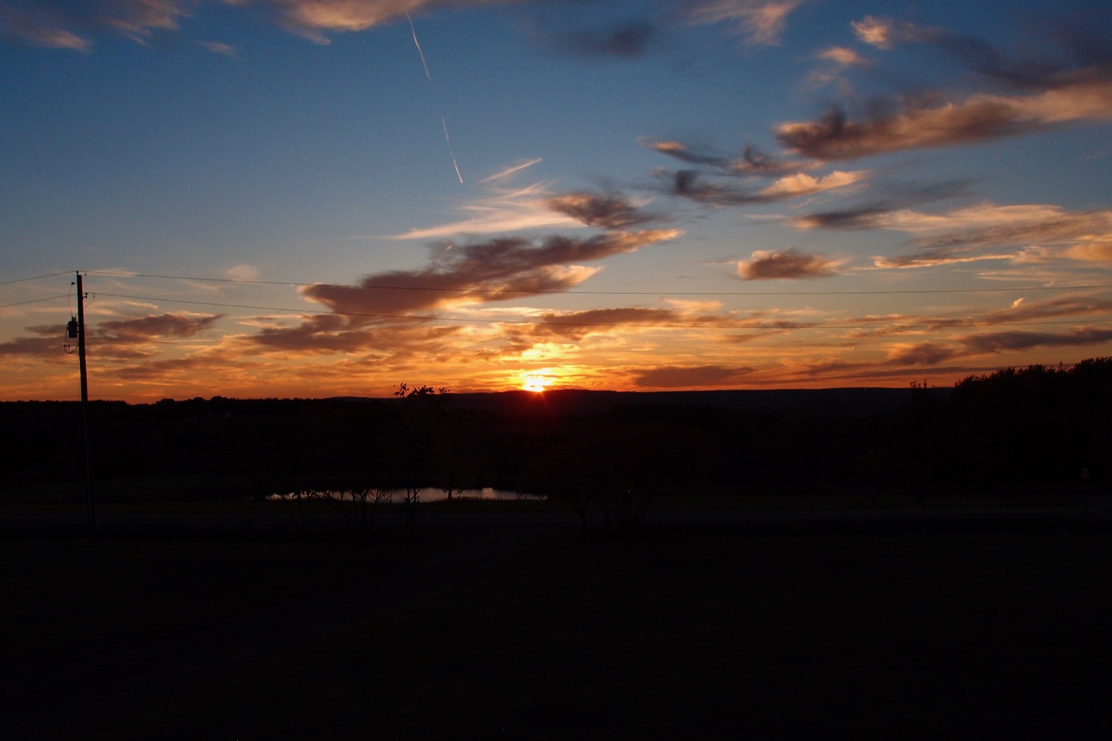 Sun setting behind distant hills illuminating clouds on the horizon