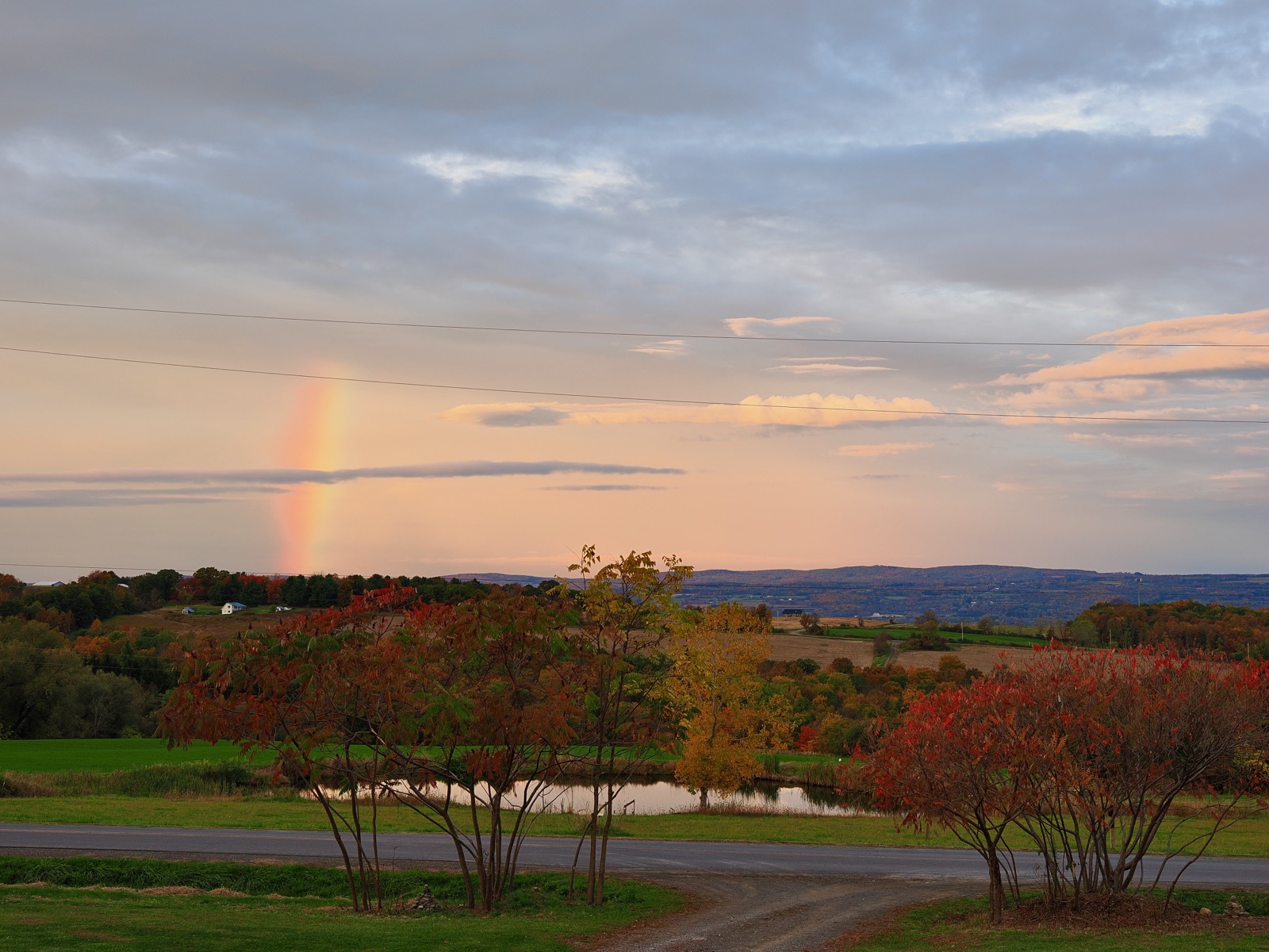 Partial rainbow against the horizon of a rural landscape with low clouds and fall colors