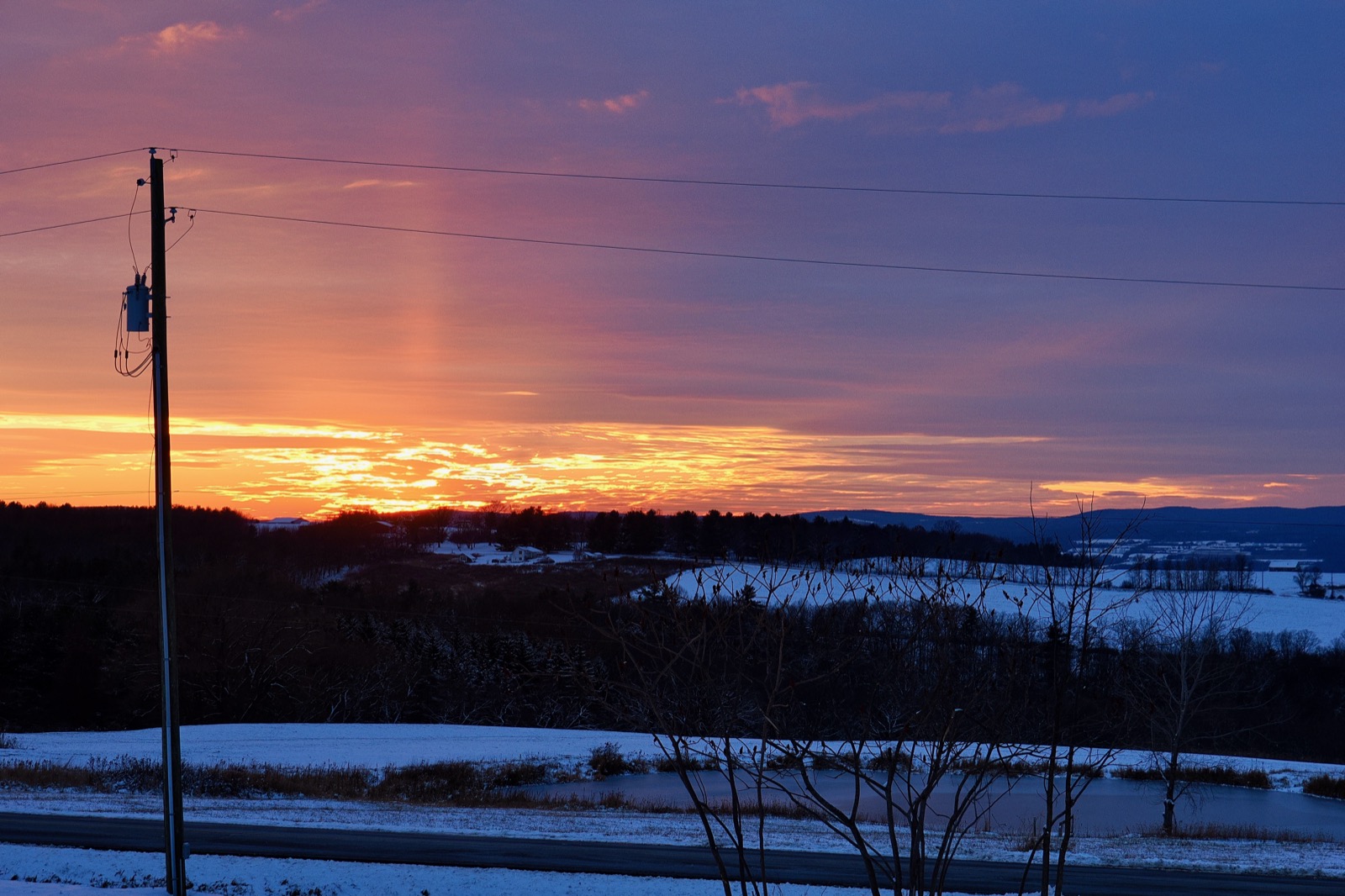 Telephoto image of the sunset beneath a a distant hill