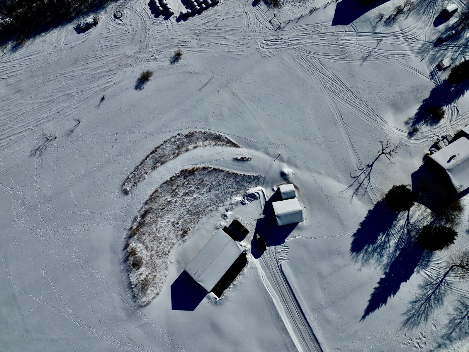 Overhead drone shot of a house in a snow-covered rural landscape revealing hundreds of animal tracks.