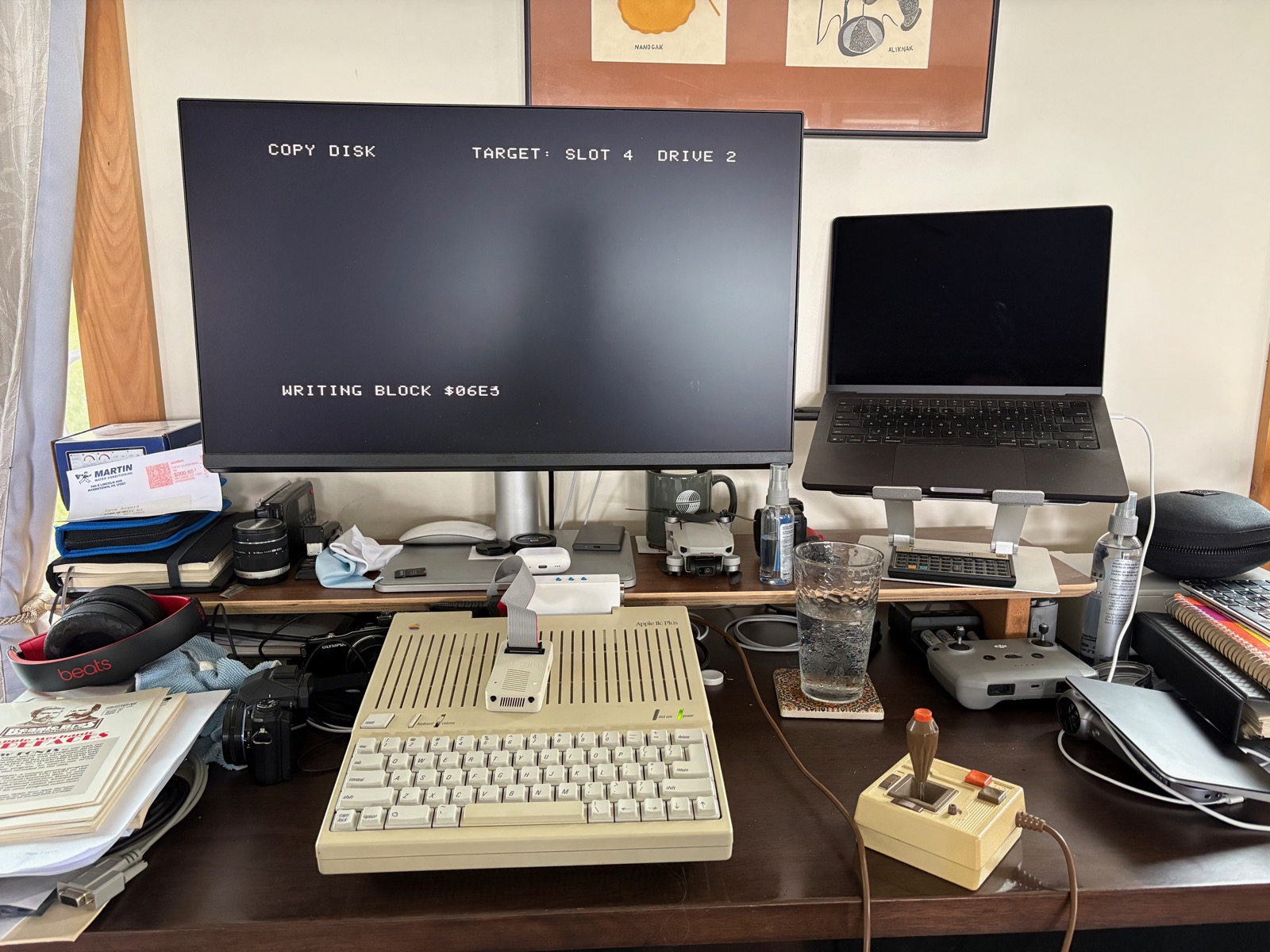 Cluttered desk with an Apple IIc, LCD screen and assorted crap on it.