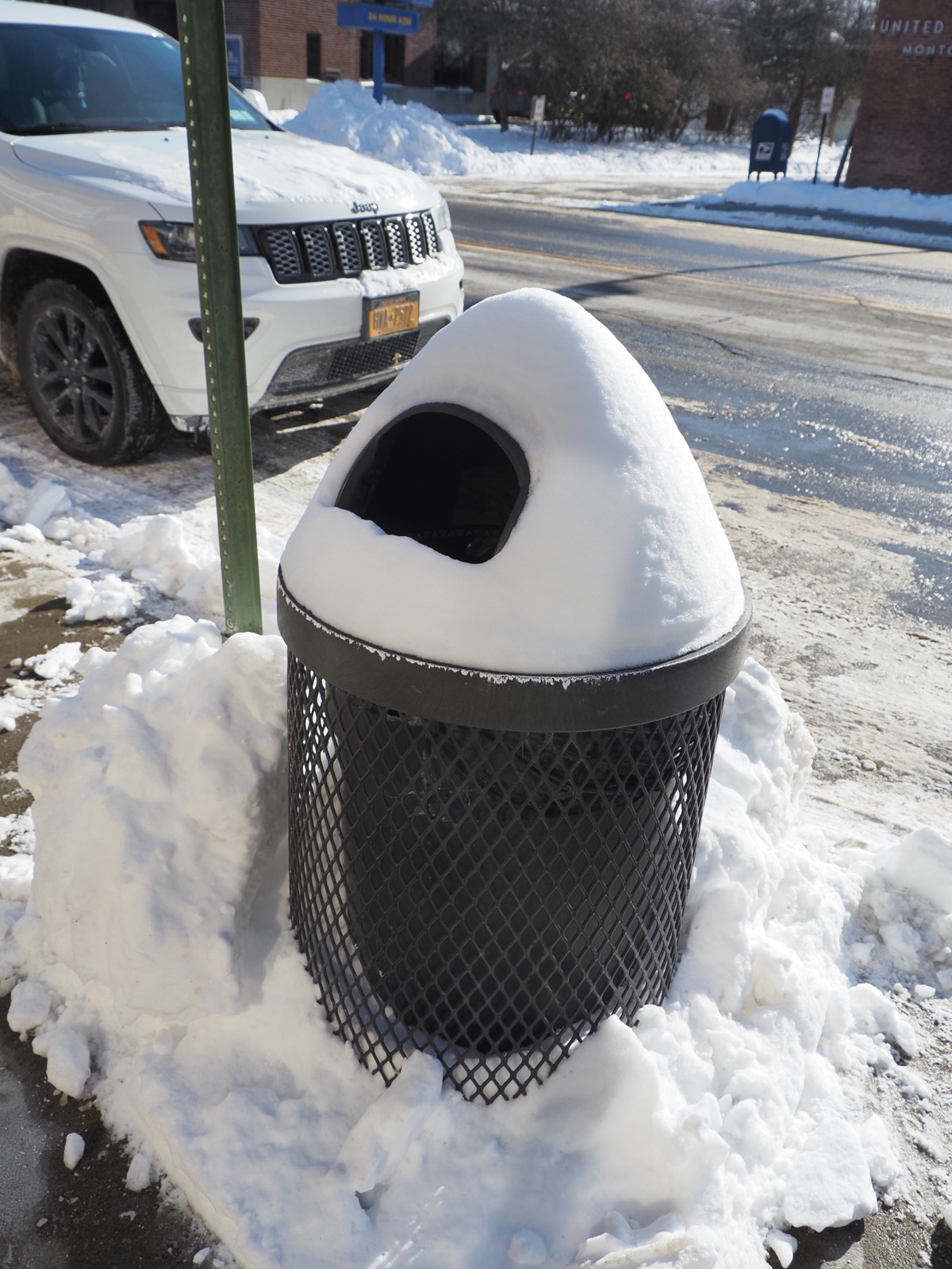 Snow accumulated into a cone shape on top of a garbage can