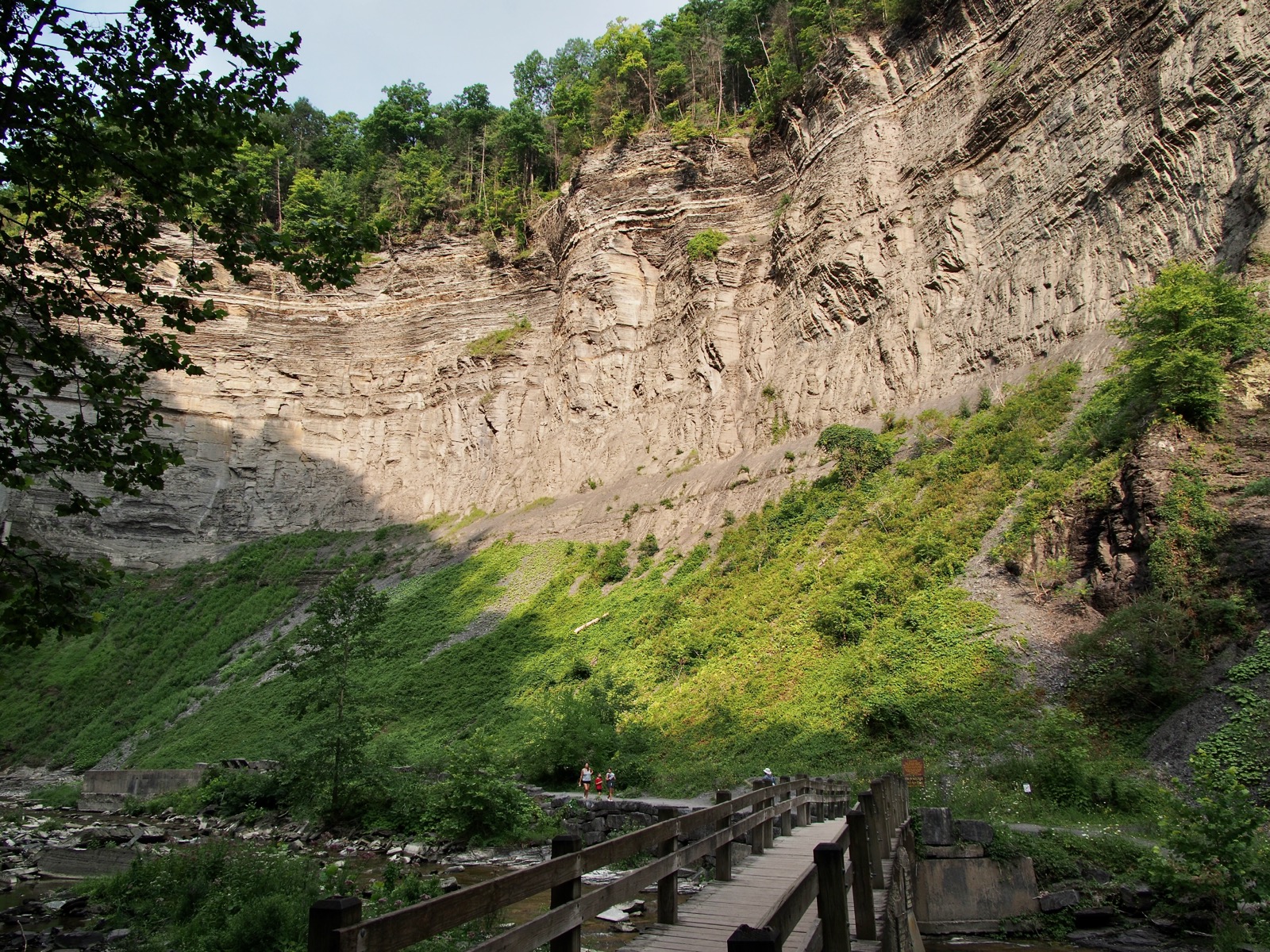 Image of the northwest wall of the gorge at Taughannock Falls with a wooden foot bridge in the foreground.