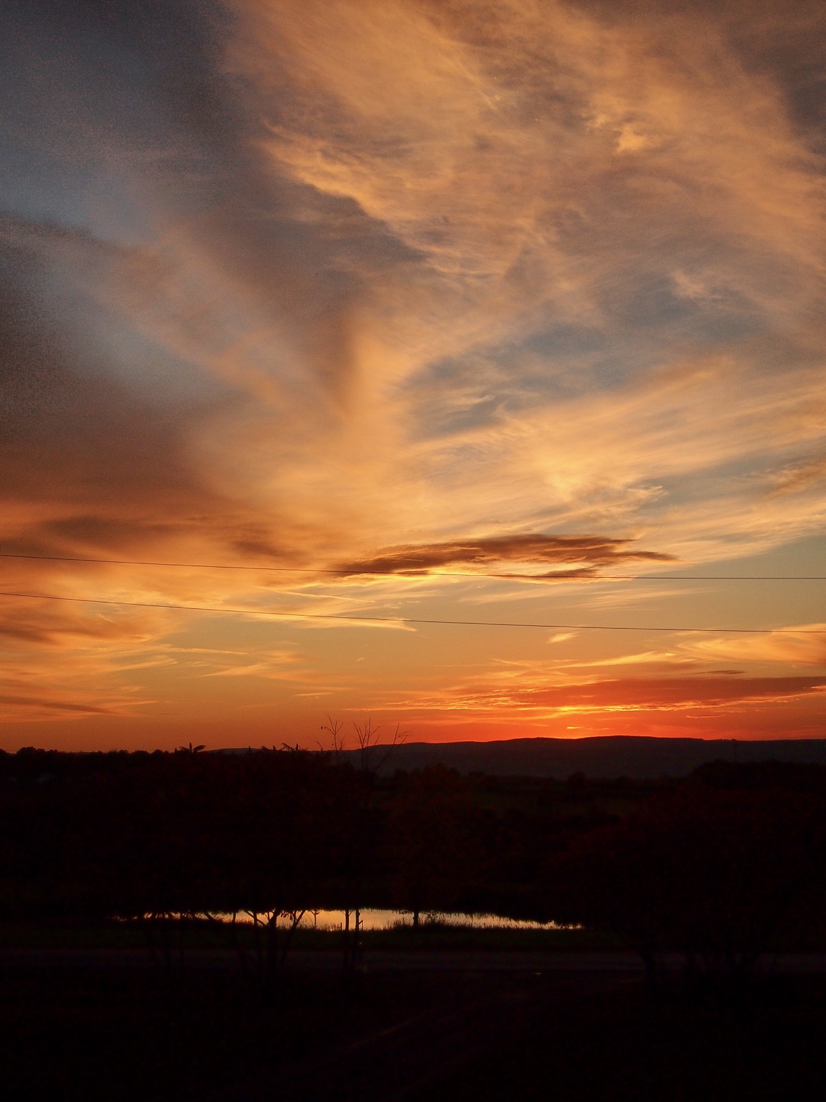 Diaphanous clouds illuminated in red and gold by the setting sun.