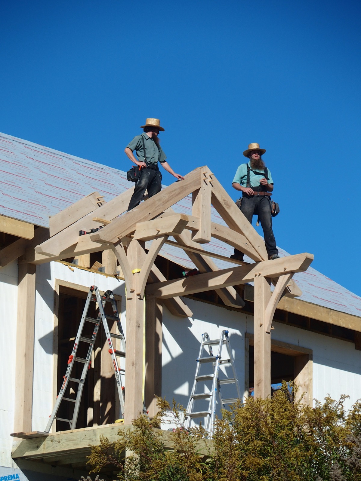 Two workmen in straw hats and suspenders standing atop a timber frame porch